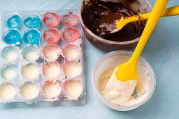 The process of making handmade chocolates. A candy mold with colorful dyes and bowls with white and dark chocolate.
