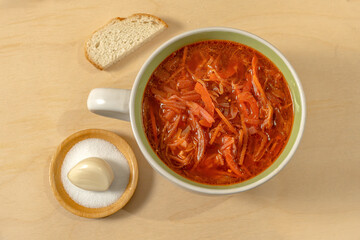 Vegetable soup in a soup bowl with bread, salt and garlic on a wooden background. Cabbage soup. Borsch. Top view