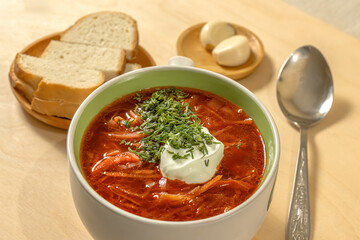 Vegetable soup without meat with sour cream and greens in a plate with bread, salt and garlic on a wooden background. Cabbage soup. Borsch