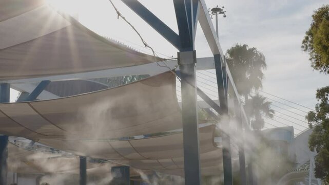 Water vapor is being sprayed from a series of nozzles on a metal structure with a fabric roof in an ef to keep tourists cool