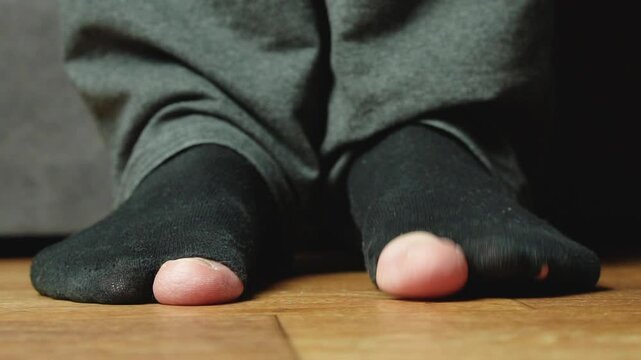 A man's feet in old black socks with holes in the big toe