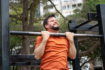 Hombre entrenando, haciendo dominadas en barra en un parque público