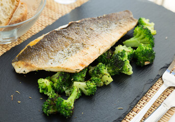 Fried fillet of sea bass with garnish of broccoli on black warm stone plate