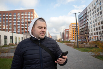 Man using smartphone outdoors in city, connected to wifi, typing messages while walking along an avenue.