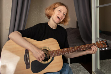 Woman Practicing Acoustic Guitar in Cozy Bedroom, engaged in music practice and chord mastery, a personal lifestyle and leisure pursuit.