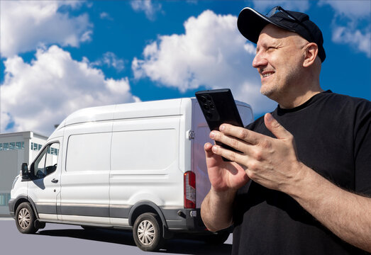 Man driver of logistics van. Car for delivering goods. Courier with phone near warehouse building. Van driver calls supplier. Man contractor for logistics company. Delivery van behind courier