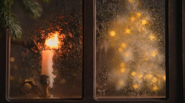 a candle is lit candle on a windowsill next to a frosted window pane with a christmas tree made of string lights glowing behind it during a cold winter night, hope