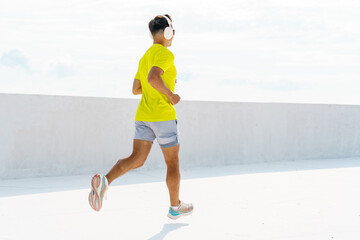 Man jogs on a roof terrace while listening to music on a sunny day in a vibrant yellow shirt