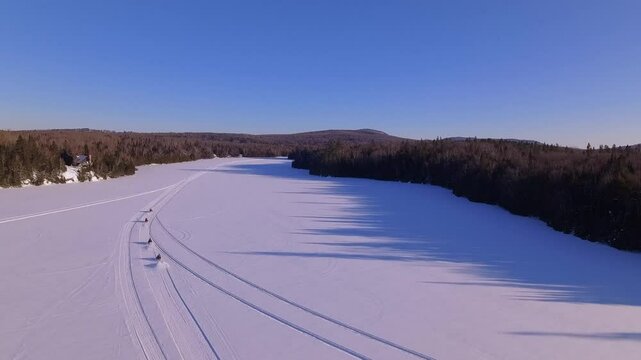 Drone footage of people riding snowmachines in a row on the frozen Lac des Grandes Baie Lake