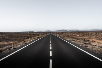 Expansive road stretches through arid landscape under a clear sky