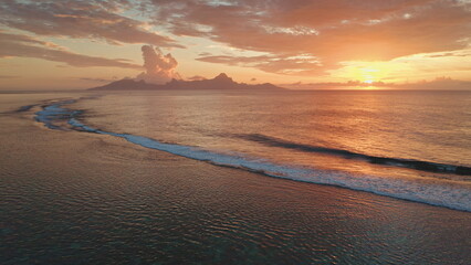 Golden sunset colorful sky over the ocean waves rolling towards the beach shore, picturesque tropical scene in Tahiti, French Polynesia. Remote wild nature paradise, exotic summer travel background