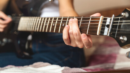 Close-up of a women playing a guitar on a bed. Guitar strings visible. Relaxed atmosphere with an...