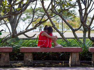 A sad little girl is sitting alone on bench in park. The little girl is unhappy and anxious because...