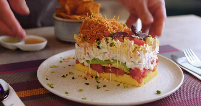 Closeup slow-motion footage of waiter's hands while serving a Peruvian Causa in a restaurant