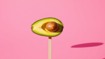 A half avocado on a stick against a pink background