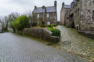 Une ruelle de Locronan, les pavés mouillés miroitent sous une lumière douce, et les maisons de...