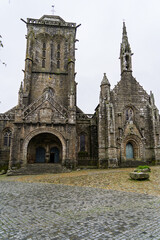 Obraz premium L'église de Locronan sous un ciel gris d'automne, ses pierres humides se détachent dans la lumière tamisée, donnant un air mystérieux à l'ensemble.