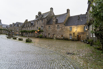 Une place pittoresque de Locronan, entour&eacute;e de maisons en pierre typiques. Le ciel gris d'automne et les pav&eacute;s mouill&eacute;s cr&eacute;ent une ambiance tranquille et chaleureuse.