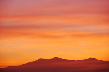 Early morning light sky before sunrise. Vivid warm yellow, orange and brown light on mountainous horizon. Panoramic sky with colorful pastel tone colors for background.