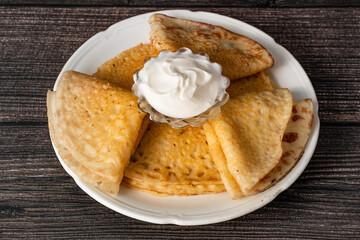 Pancakes are on a white plate, they have a bowl with sour cream on a wooden table