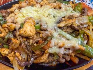 Closeup Of Chicken And Beef Fajitas Covered With Cheese On An Iron Skillet