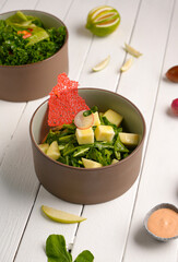 Fresh arugula and apple salad, with dressing and garnish, white wooden background