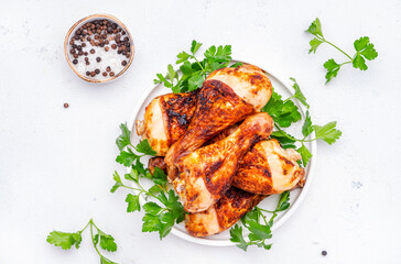 Baked chicken legs or drumsticks in spices with parsley on plate, white table background, top view