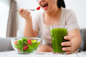 Beautiful Asian woman eating salad, holding a glass bowl and using a fork to pick up a tomato to eat