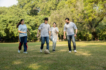 A lively and candid capture of a family enjoying a soccer game in the park. The parents, alongside their two daughters, laugh and play as they chase the soccer ball on the grass.