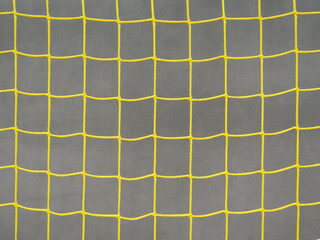 Close-up of yellow soccer goal net: geometric mesh against gray protective wall in a sports hall with retro charm.