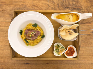 Beef rendang fried rice with turmeric herbs and curry sauce. Served with prawn crackers, marinated cucumber, and chili sauce dressing, on a wooden tray, on a wood rustic table.