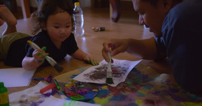 A Asian father and young daughter child engage in creative painting on the floor in cozy home, fostering imagination and bonding in a warm home setting.