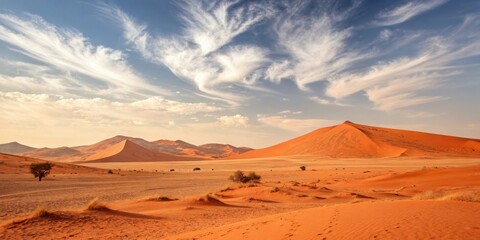 Naklejka premium A vast, red desert landscape with towering dunes reaching for a sky adorned with delicate, white clouds.