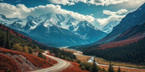 A winding asphalt road snakes through a valley, flanked by vibrant autumn foliage and towering snow-capped mountains under a sky of fluffy white clouds.