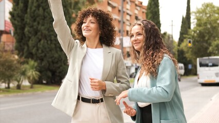 Happy businesswomen signaling taxi near street in city