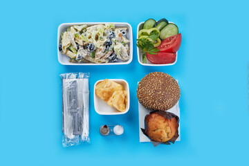 top shot closeup on soft blue background there are disposable tableware food for airplanes snack disposable set salt and pepper pasta with vegetables omelet bagel bun light cupcake vegetable salad
