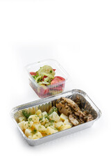white background disposable plastic and foil tableware airplane food snack boiled potatoes sprinkled with dill with pieces of chicken fillet and salad of fresh sliced cucumbers and tomatoes