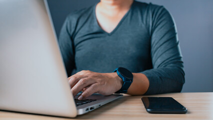 A person types on a laptop while a smartphone rests on a table, symbolizing technology, work, communication, and modern productivity in a professional or home office setting.