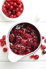 Tasty cranberry sauce in gravy boat and berries on white wooden table, top view