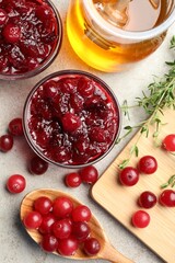Tasty cranberry sauce in glass bowls, berries, thyme and honey on light table, flat lay