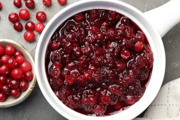 Tasty cranberry sauce in gravy boat and berries on grey table, top view