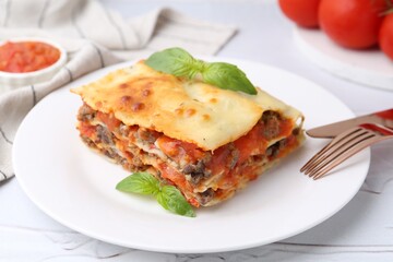 Piece of delicious cooked lasagna with basil on white textured table, closeup