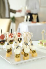 Many different tasty canapes on white table. People clinking glasses of wine indoors, closeup