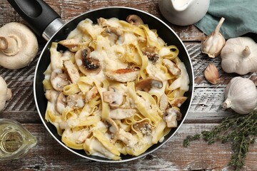 Flat lay composition with tasty Alfredo pasta with chicken and mushrooms in frying pan on wooden table