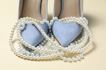 Stylish shoes and pearl necklace on beige background, closeup