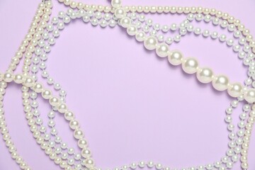 Beautiful pearl necklaces on violet background, flat lay. Space for text