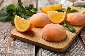Board with tasty mochi, cut orange and mint on wooden table, closeup