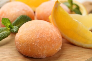 Tasty mochi, cut orange and mint on wooden board, closeup