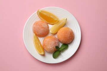 Plate with tasty mochi, cut orange and mint on pink table, top view