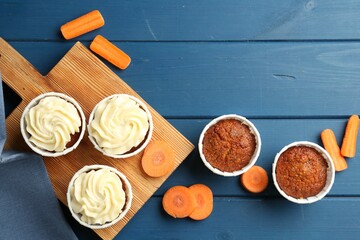 Delicious carrot muffins and fresh vegetables on blue wooden table, flat lay. Space for text